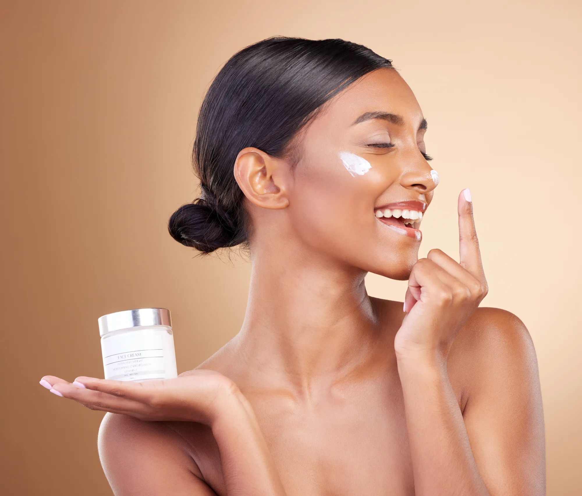 A young beautiful women is putting a beauty cream on her face, holding the facial cream in her one hand.