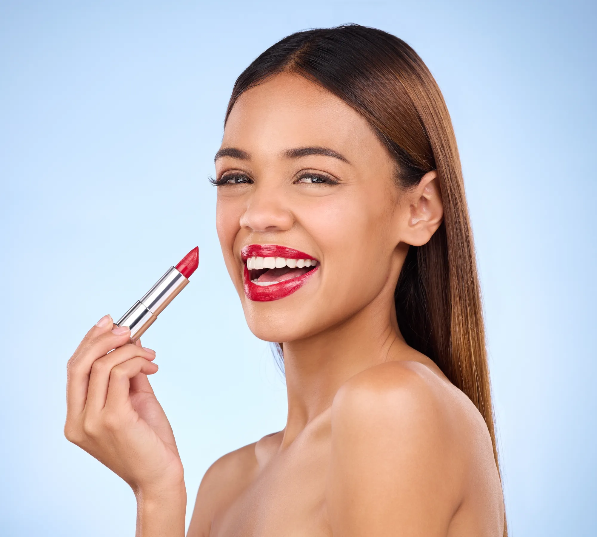 A beauty shot of a young woman with red lips holding a lipstick in her hand. 
